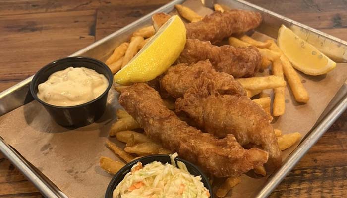 Fried fish and fries with lemon wedges, coleslaw, and tartar sauce on a tray.