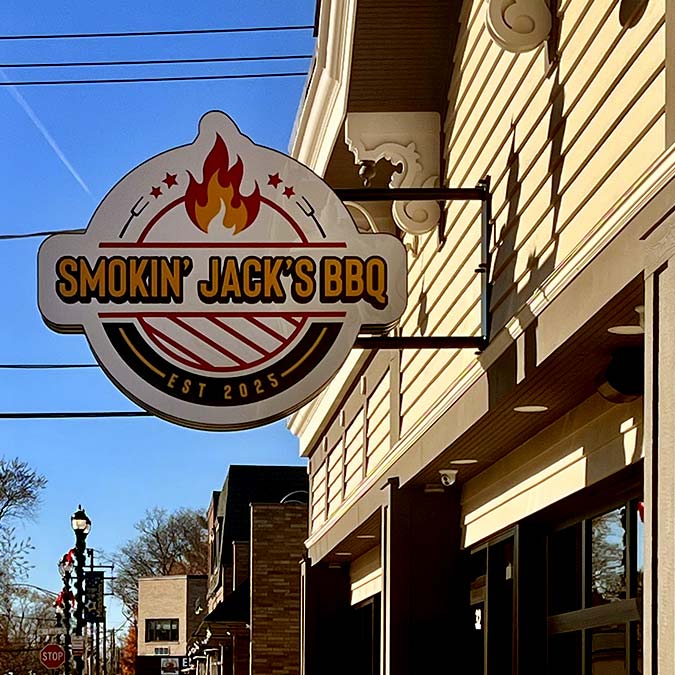A sign reads “Smokin’ Jack’s BBQ Mundelein Est 2025” with a flame and grill design above a sidewalk.