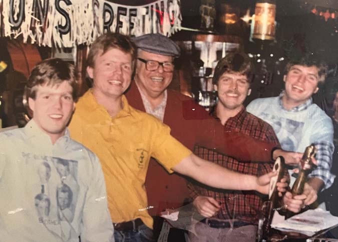 Five smiling men pose at Smokin’ Jack’s BBQ Mundelein bar, some holding beer taps, festive vibe.