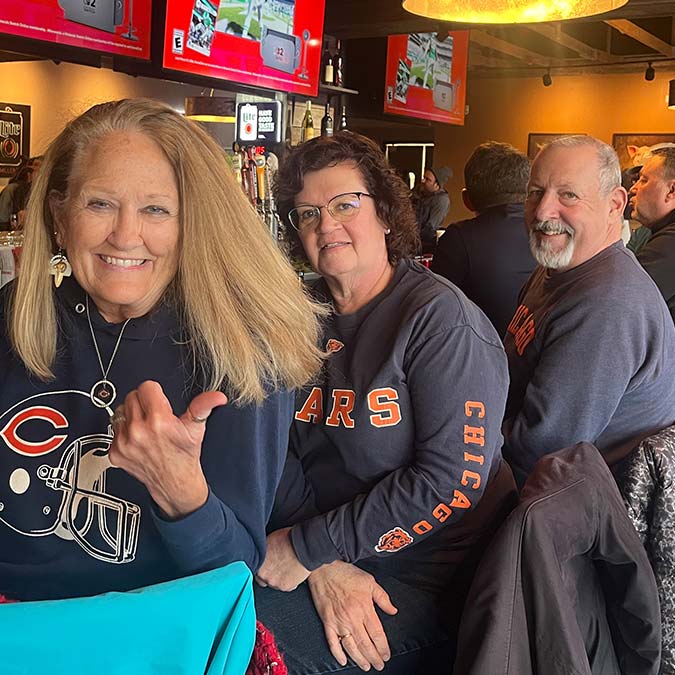 Three smiling adults at a BBQ restaurant in Mundelein IL, wearing Chicago Bears shirts at the bar.