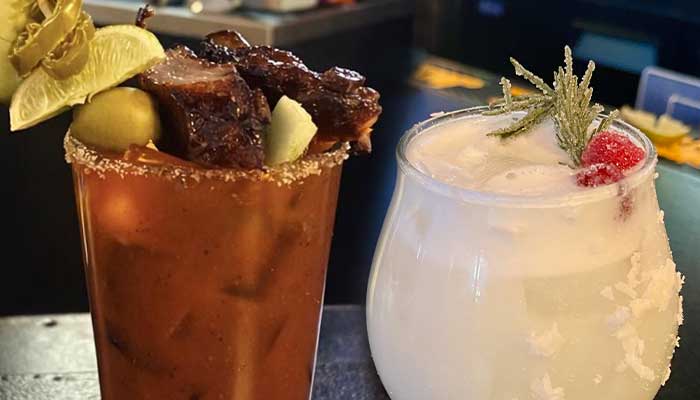 Two cocktails sit on a bar counter at a lively sports bar in Mundelein, IL.