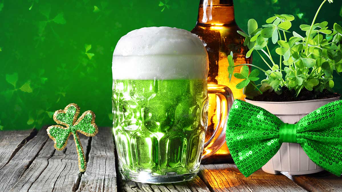 Glass of green beer, shamrock, and bow tie ready for St Patricks Day Mundelein BBQ fun.