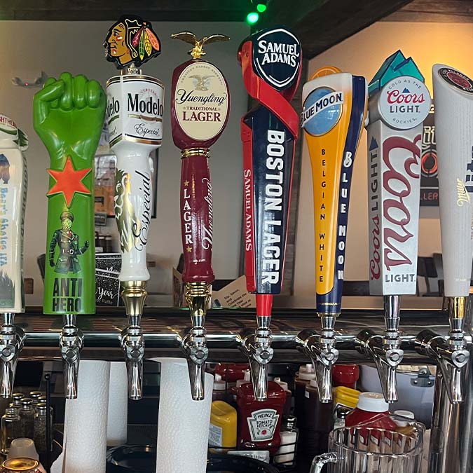 Beer taps lined up at a BBQ restaurant in Mundelein IL, each with a unique brewery and beer type.