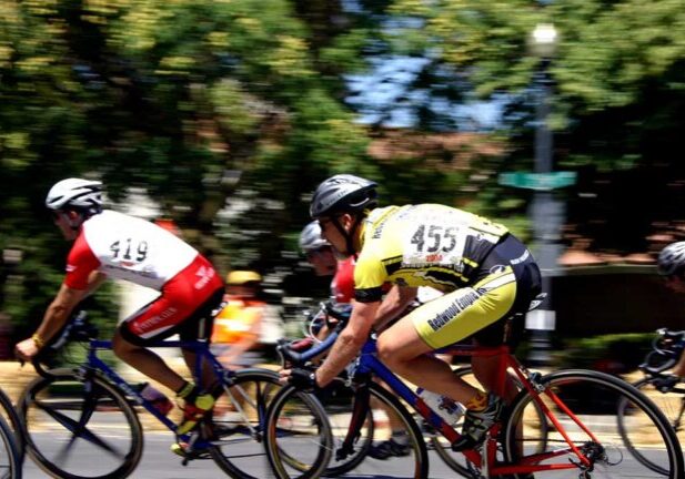 Cyclists in numbered jerseys racing on a road with trees and spectators in the background.